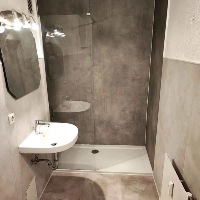 Saniertes Bad mit bodengleicher Dusche, Glaswand, Waschtisch und fugenlosen Wandflächen in Betonoptik
