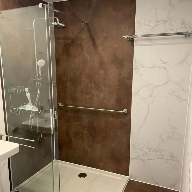 Dusche mit Wandpaneelen in Rostoptik und weißem Marmordekor, Glastür und Haltegriff