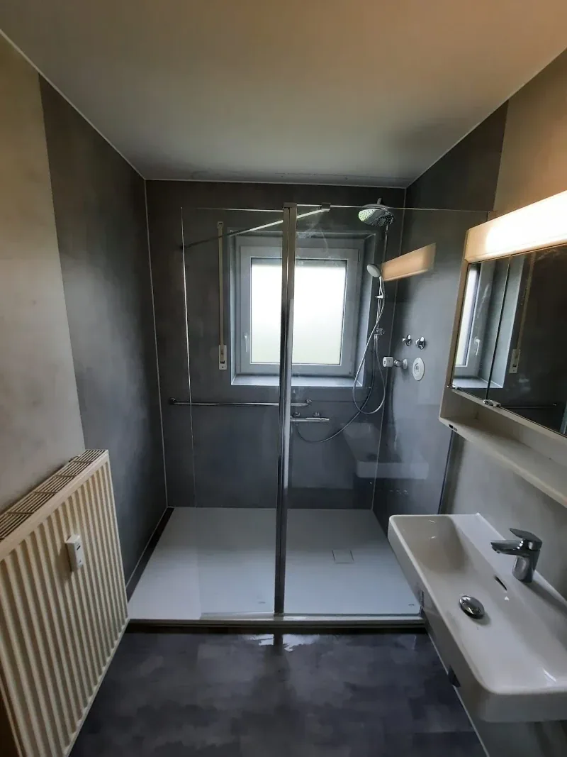 Fertiger Wannentausch mit bodengleicher Dusche, fugenlosen Wandpaneelen in Grau und Glasabtrennung